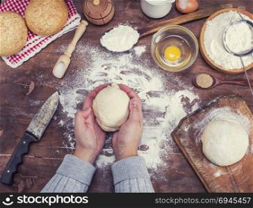 women&rsquo;s hands hold a ball of yeast dough on a table in the middle of the ingredients for bread making