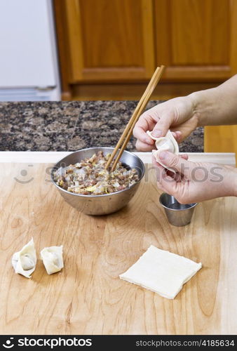 Women&rsquo;s Hands making wonton with wooden board and stainless steel bowls in kitchen