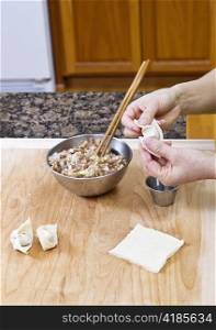 Women&rsquo;s Hands making wonton with wooden board and stainless steel bowls in kitchen