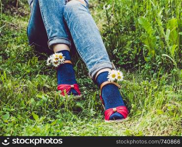 Women's legs, fashionable shoes, bright multi-colored socks on a background of green grass. Close-up. Concept of style, fashion and beauty. Women's legs, fashionable shoes and bright socks