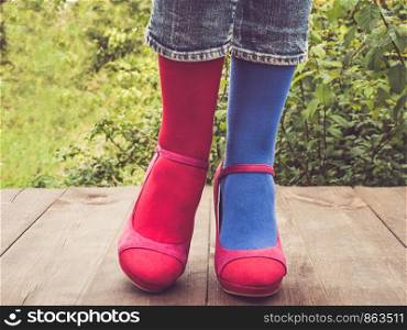 Women's legs in stylish shoes, bright, variegated, multi-colored socks on the wooden terrace on the background of green trees. Lifestyle, fashion, beauty, fun. Women's legs in stylish shoes, bright, variegated, multi-colored socks