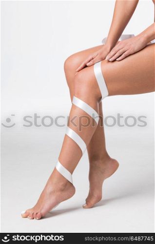 Women&rsquo;s legs with white ribbon. Closeup of perfect women&rsquo;s legs with white ribbon on white background