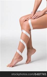 Women&rsquo;s legs with white ribbon. Closeup of perfect women&rsquo;s legs with white ribbon on white background