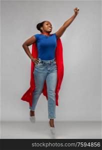 women&rsquo;s power and people concept - happy african american woman in red superhero cape over grey background. happy african american woman in red superhero cape