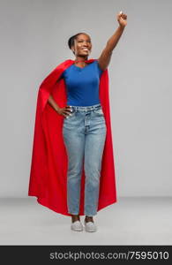 women&rsquo;s power and people concept - happy african american woman in red superhero cape over grey background. happy african american woman in red superhero cape