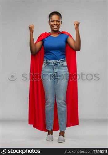 women&rsquo;s power and people concept - happy african american woman in red superhero cape over grey background. happy african american woman in red superhero cape