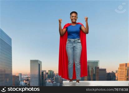 women&rsquo;s power and people concept - happy african american woman in red superhero cape over tokyo city skyscrapers on background. happy african american woman in red superhero cape
