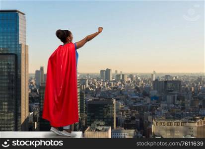 women&rsquo;s power and people concept - happy african american woman in red superhero cape over tokyo city skyscrapers on background. happy african american woman in red superhero cape