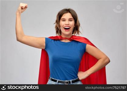 women&rsquo;s power and people concept - happy woman in red superhero cape showing arm bicep muscle over grey background. happy woman in red superhero cape showing power