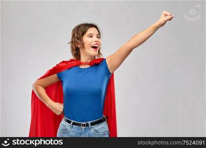 women&rsquo;s power and people concept - happy woman in red superhero cape making flying pose over grey background. happy woman in red superhero cape