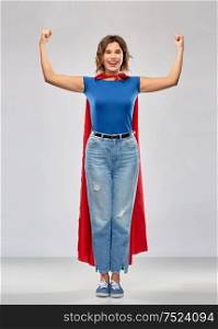women&rsquo;s power and people concept - happy woman in red superhero cape showing arm bicep muscle over grey background. happy woman in red superhero cape showing power