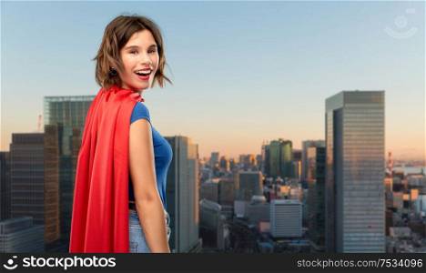women&rsquo;s power and people concept - happy woman in red superhero cape over evening tokyo city skyscrapers background. happy woman in red superhero cape over tokyo city