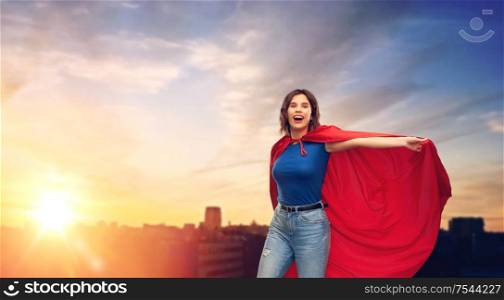 women&rsquo;s power and people concept - happy woman in red superhero cape over sunset in city background. happy woman in red superhero cape over city sunset