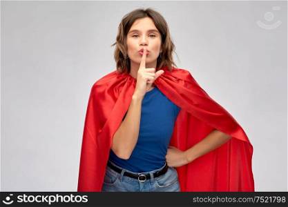 women&rsquo;s power, silence and secret concept - happy woman in red superhero cape making hush gesture over grey background. happy woman in red superhero cape