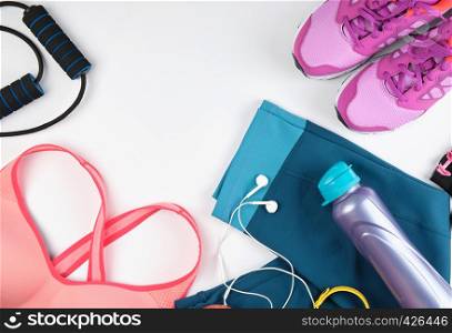 women's sportswear for fitness, a bottle, headphones and sneakers on a white background, top view, copy space
