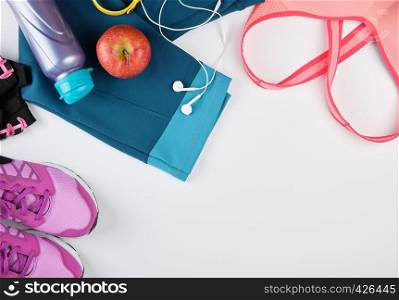 women's sportswear for fitness, bottle, headphones and sneakers on a white background, top view, copy space