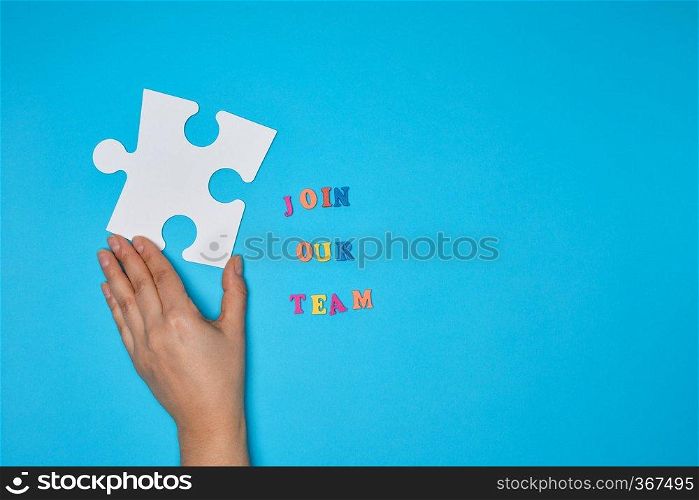 women’s hand hold  large white puzzle and the inscription join our team on a blue background, the concept of recruitment, copy space 