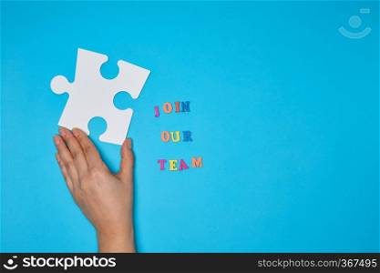 women’s hand hold  large white puzzle and the inscription join our team on a blue background, the concept of recruitment, copy space 