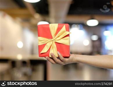 Women’s hand holding a red gift box on Blur restaurant background Concept of love and Valentine’s Day.