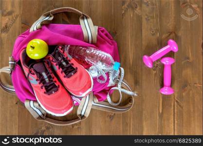 Women's sports bag with objects and clothes for a workout on a dark floor view from above