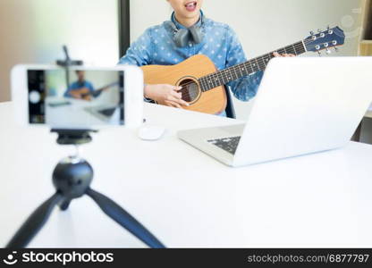 women sing a song with guitar in hands use camera to broadcast live video to social network by internet at home