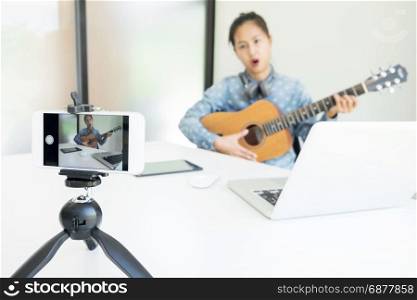 women sing a song with guitar in hands use camera to broadcast live video to social network by internet at home