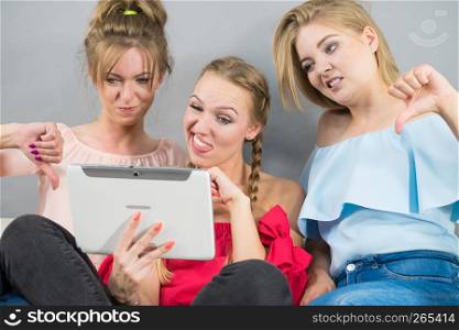 Women sitting on sofa having fun surfing on the internet using smart digital pc tablet modern device judging something. Three women using tablet