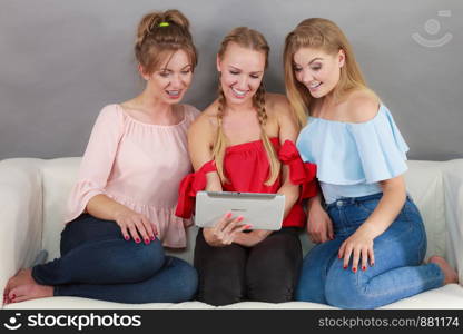 Women sitting on sofa having fun surfing on the internet using smart digital pc tablet modern device. Three women using tablet