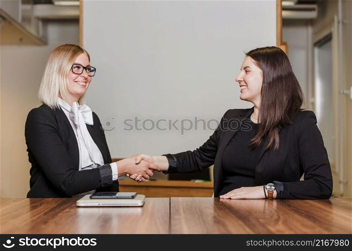 women sitting table shaking hands smiling