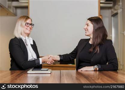 women sitting table shaking hands smiling