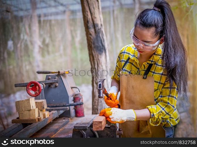 Women standing builder wearing checked shirt worker of construction site hammering nail in the wooden board
