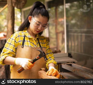 Women standing builder wearing checked shirt worker of construction site hammering nail in the wooden board