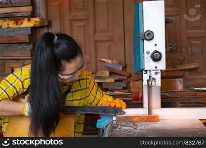 Women standing is craft working cut wood at a work bench with band saws power tools at carpenter machine in the workshop, Worker sawing boards from with sawmill wood processing a family business