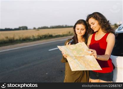 women standing near white car looking map