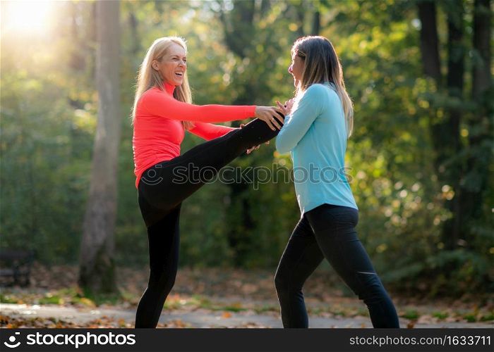 Women Stretching with Personal Fitness Trainer After Training in The Park.