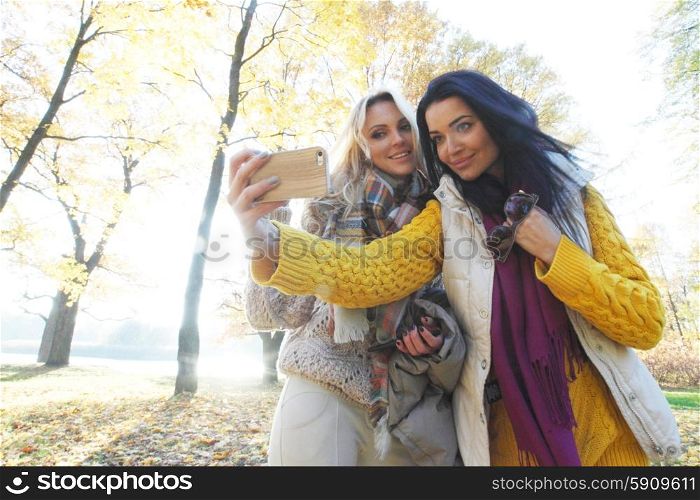 Women taking selfie in park. Beautiful young women taking a selfie with smartphone outdoors in park in autumn