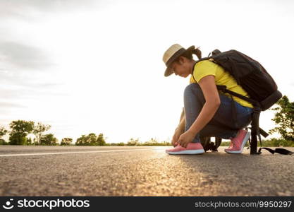 Women tourists tying the sneakers on the highway with the golden light of the sun, backpacker concept.