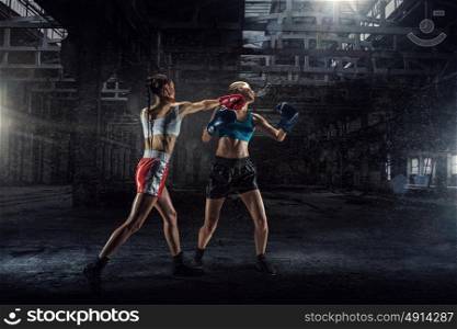 Women ultimate fighting. Two young pretty women boxing in desolate building. Mixed media