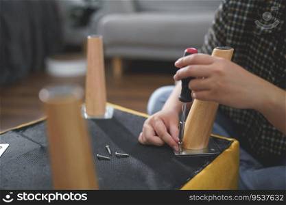 Women use screwdriver equipment to tighten screw while assembling leg of chair to making furniture.