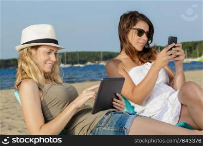 women use touchpad tablet technology on the beach