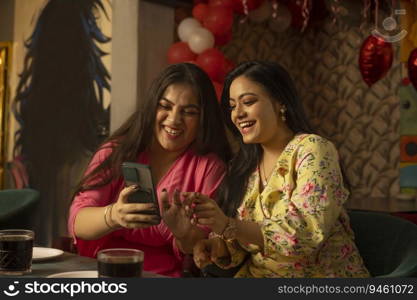 Women using mobile phone while sitting together at restaurant