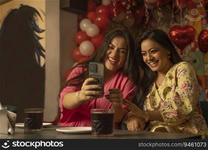 Women using mobile phone while sitting together at restaurant