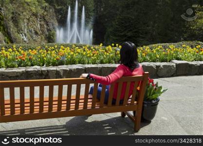 Women watch water fountain while resting on cedar bench in flower garden