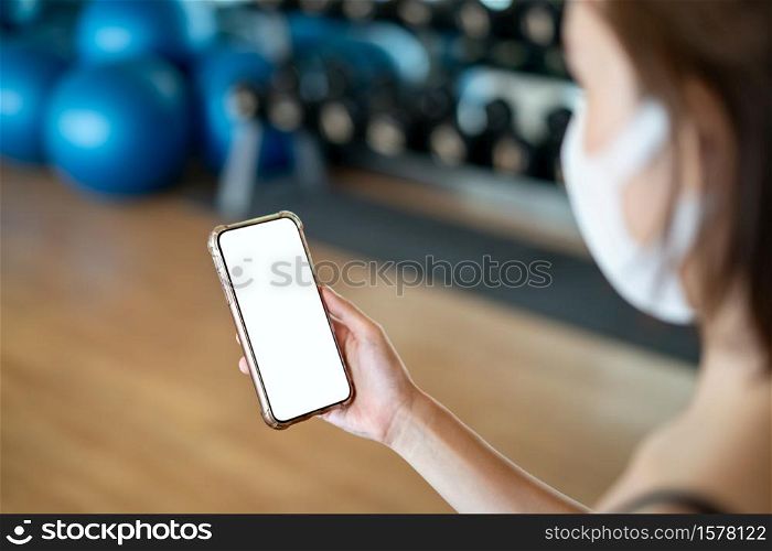 Women wearing mask making holding mockup mobile phone in the gym.