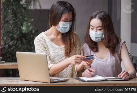 Women wearing masks and using credit card for doing online shopping in the internet. New Normal and Finance Concept.