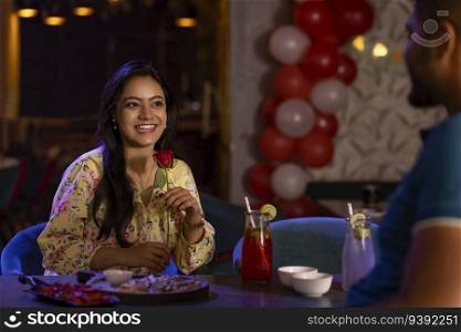 Women with a red rose sitting with her boyfriend at a restaurant