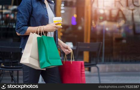 Women with coffee cup in hand and holding shopping bag while walking on the shopping mall background.