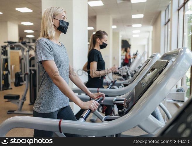 women with medical masks using gym equipment