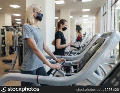 women with medical masks using gym equipment