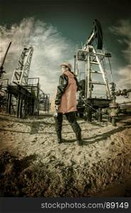 Women worker in the oil field, with wrenches in a hands, orange helmet and work clothes. Industrial site background. Toned.. Oil and gas industry worker.
